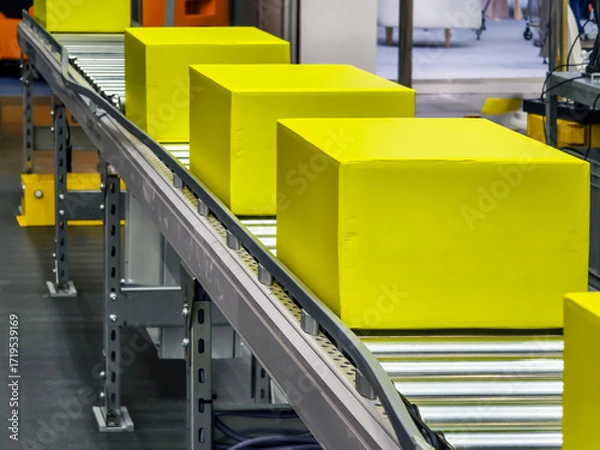 Fototapeta Bright yellow boxes moving along a conveyor belt in a busy warehouse setting