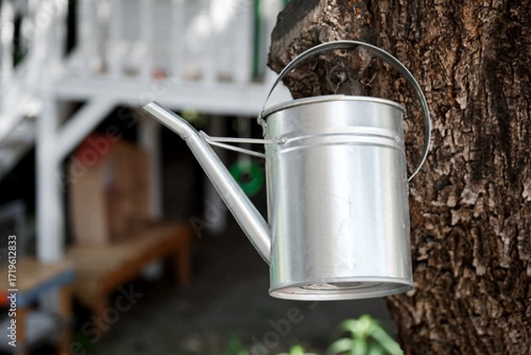 Fototapeta Metal Watering Can Hanging on a Tree Trunk in a Garden