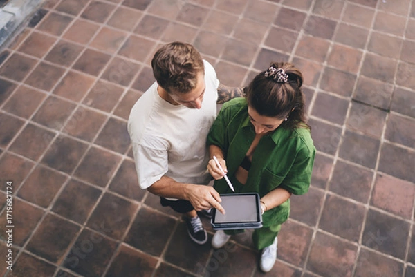 Fototapeta Focused creative duo standing close with tablet and stylus, visually interpreting design solutions, embracing smart collaboration and shared responsibility in tech creation.