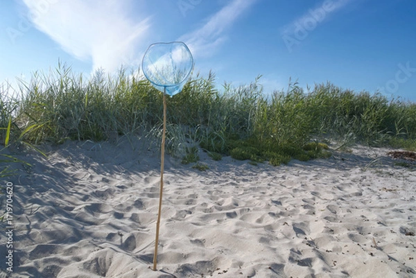 Fototapeta Blue landing net with wooden pole on a sandy beach, with a blue sky. Vacation