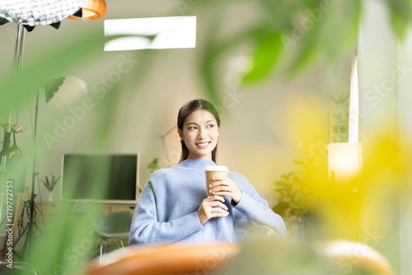 Fototapeta Young Asian woman enjoying a peaceful moment reading a book near window. Calm lifestyle, self-learning, and mindfulness at home.