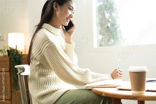 Fototapeta Young Asian woman enjoying a peaceful moment reading a book near window. Calm lifestyle, self-learning, and mindfulness at home.