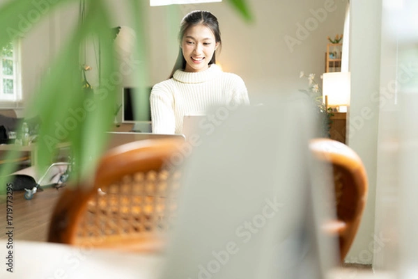Fototapeta Young Asian woman enjoying a peaceful moment reading a book near window. Calm lifestyle, self-learning, and mindfulness at home.