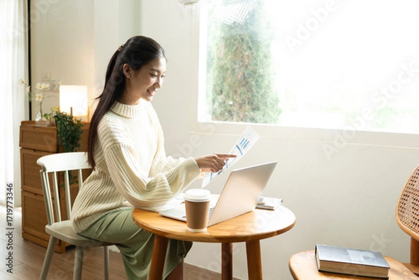 Fototapeta Young Asian woman enjoying a peaceful moment reading a book near window. Calm lifestyle, self-learning, and mindfulness at home.