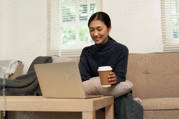 Fototapeta Young Asian woman enjoying a peaceful moment reading a book near window. Calm lifestyle, self-learning, and mindfulness at home.