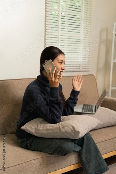 Fototapeta Young Asian woman enjoying a peaceful moment reading a book near window. Calm lifestyle, self-learning, and mindfulness at home.
