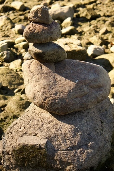 Fototapeta Balancing stones stacked in a pyramid on a dry rocky riverbed. A symbol of balance, calmness, and meditation in harmony with nature and silence.