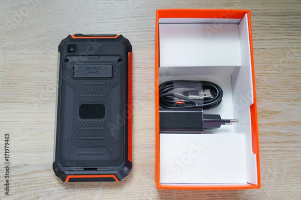 Obraz New black-orange rugged smartphone with box, charger and cable -