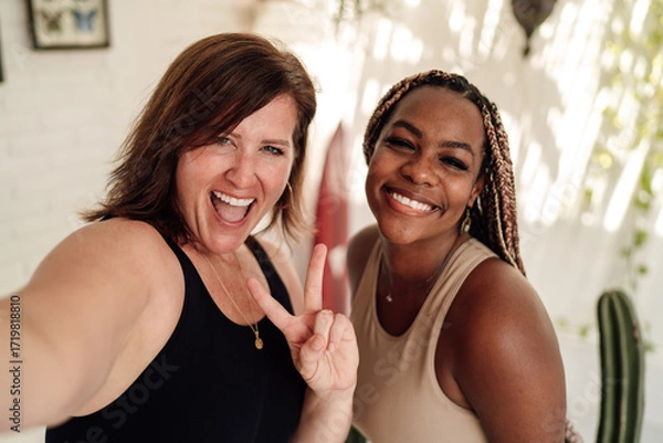 Fototapeta Happy diverse women laugh and make peace sign while taking selfie, reflecting joy, tech interaction and vibrant connection through mobile culture.