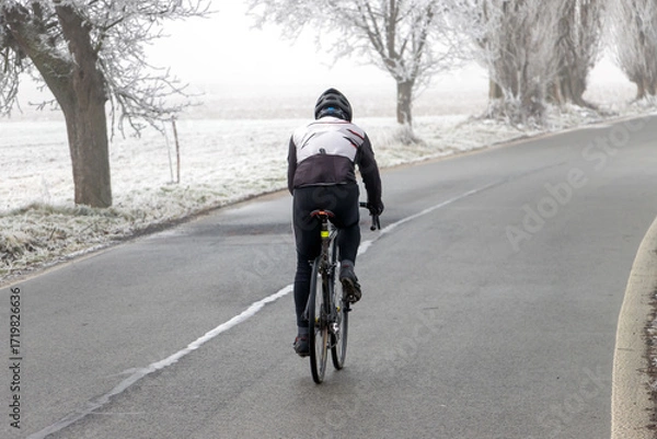 Fototapeta Cyclist riding on a frosty winter road surrounded by bare trees