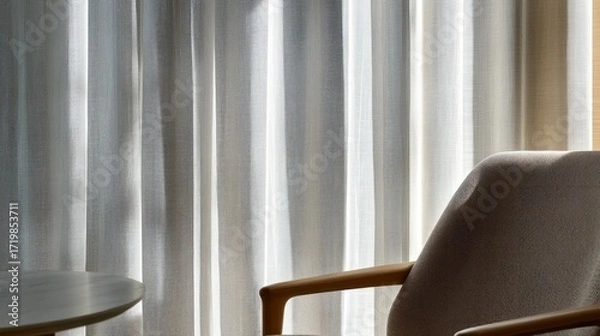 Fototapeta Soft light streams through sheer curtains, illuminating a neutral-toned armchair