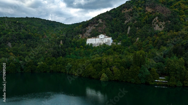 Fototapeta Aerial view of abbey of San Michele surrounded by trees. It is a Benedictine Abbey located at the foot of Monte Vulture, on the flank of the Monticchio Lake Piccolo, in Basilicata, Italy.