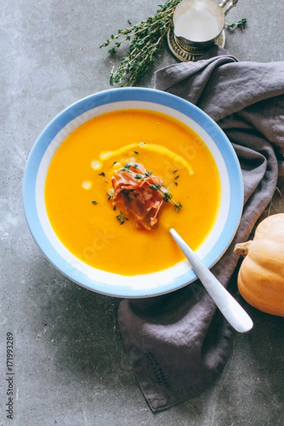 Fototapeta A plate of pumpkin soup with cream, prosciutto and thyme, on a gray background, top view