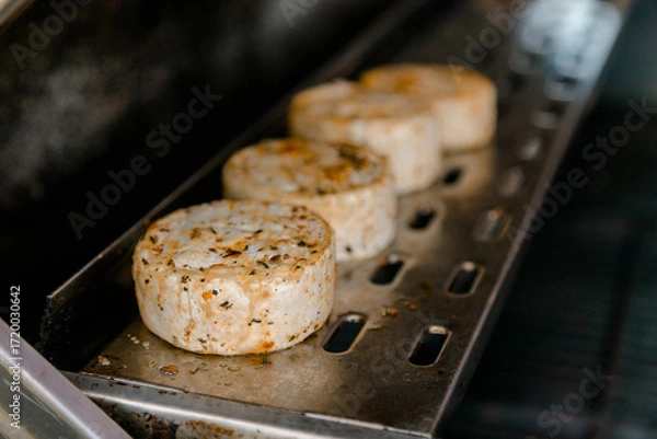 Fototapeta Grilled cheese patties with herbs and spices cooking on a metal tray, rustic and appetizing food concept