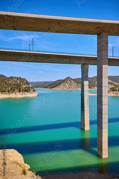 Fototapeta Tranquil scenery under a bridge over a reservoir with crystal clear turquoise water
