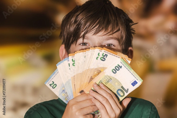 Fototapeta Smiling boy proudly holding a fan of euro banknotes in 20, 50, and 100 denominations, symbolizing wealth, savings, finance, and prosperity.