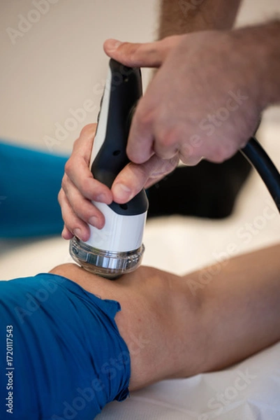 Fototapeta Physiotherapist using shockwave therapy device on knee