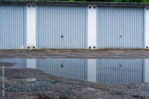 Fototapeta Row of white garages mirrored in a broad roadside puddle