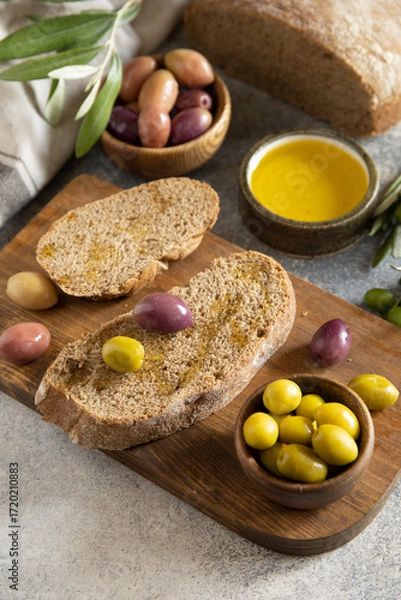 Fototapeta Mediterranean snack with mixed olives, olive oil, and rustic bread on wooden board. Copy space.