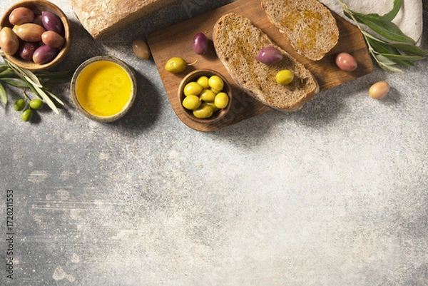 Fototapeta Mediterranean snack with mixed olives, olive oil, and rustic bread on wooden board. Top view.