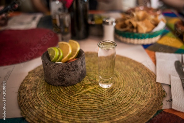 Fototapeta Frontal photo of a delicious crystalline mezcal in its glass caliber, accompanied by worm salt, oranges, and lemon served in a small molcajete.

