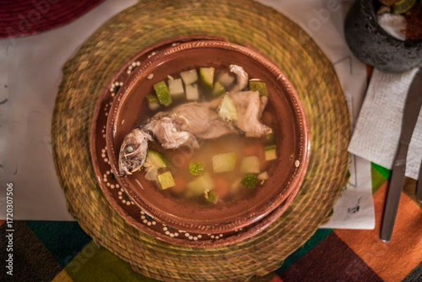 Fototapeta Cenital photo of Rat broth, a typical dish from the state of Zacatecas, Mexico, accompanied by chopped vegetables and a whole field rat, served in a clay dish.

