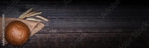 Fototapeta Fresh round bread on black wooden board, view with copyspace. Long banner