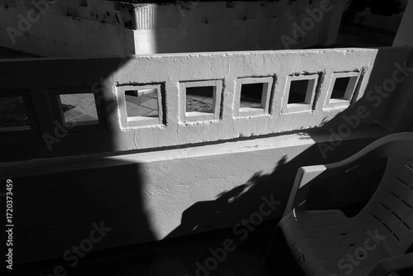 Fototapeta Black and white image of a concrete wall with small square windows casting strong shadows, emphasizing geometric patterns and contrast