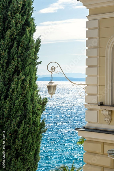 Fototapeta Elegant seaside view with a classic lamp, cypress tree, and shimmering blue sea in Opatija Croatia