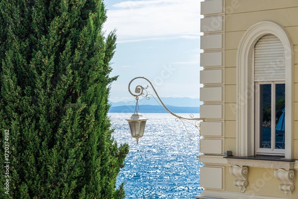 Fototapeta Elegant seaside view with a classic lamp, cypress tree, and shimmering blue sea in Opatija Croatia