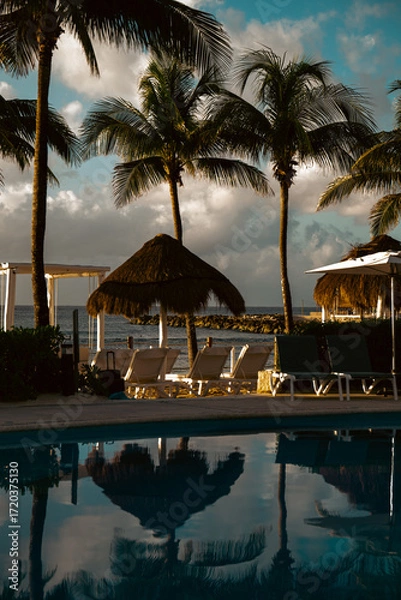 Obraz Tropical resort pool reflecting palm trees and clouds in stunning sunset hues.