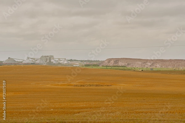 Fototapeta A potash plant with multiple dome-shaped storage buildings and conveyors viewed across farmland under cloudy skies in Saskatchewan, Canada.