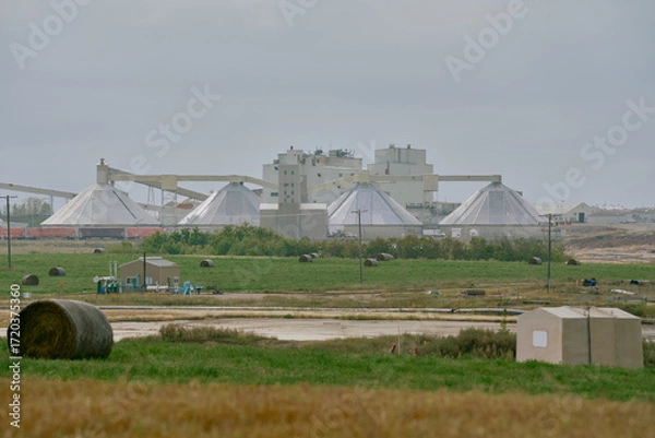 Fototapeta Industrial potash processing plant in Saskatchewan, Canada, with large domed storage structures, pipelines, and construction equipment in the foreground under cloudy skies.