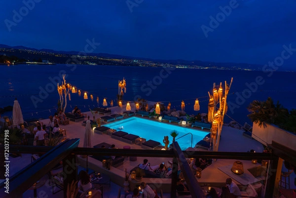 Fototapeta Chic seaside rooftop lounge with glowing pool, lanterns, and ocean views in Opatia Croatia