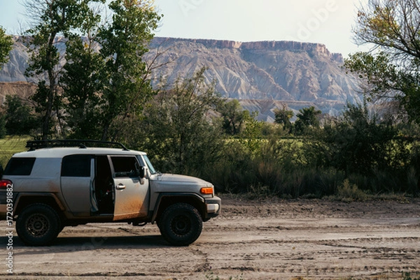 Obraz Off-road vehicle parked by lush greenery against a striking rock backdrop.