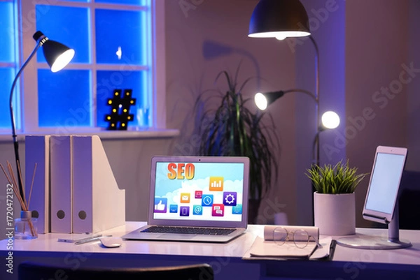 Fototapeta Laptop with abbreviation SEO on desk in dark office