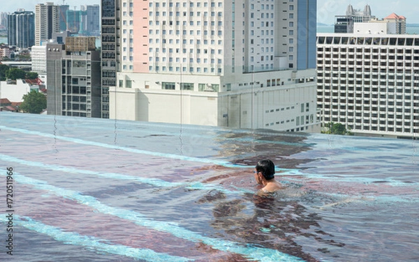 Fototapeta Man swimming in infinity roof top pool. City view at the background.