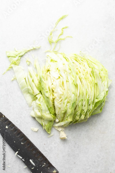 Fototapeta Overhead view of sliced cabbage on a marble countertop, top view of cabbage leaves being shredded, green cabbage being sliced