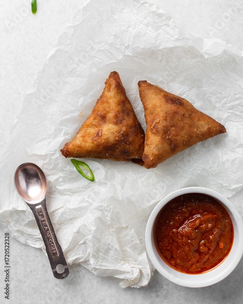 Fototapeta Overhead view of samosa with dip on parchment paper, top view of beef samosa on a white background