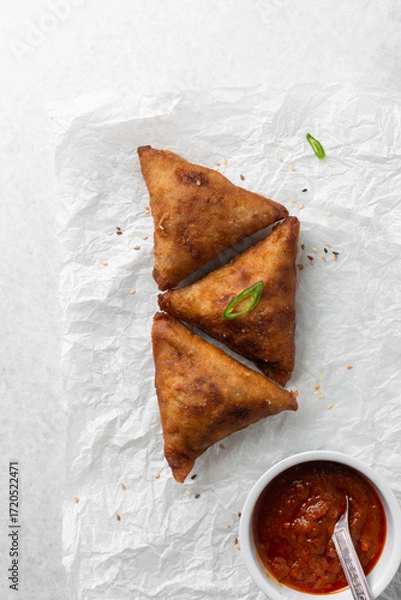 Fototapeta Overhead view of samosa with dip on parchment paper, top view of beef samosa on a white background