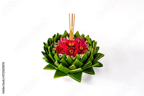 Fototapeta Banana leaf Krathong that have 3 incense sticks and candle decorates with pink flowers for Thailand full moon or Loy Krathong festival isolated on white paper background.