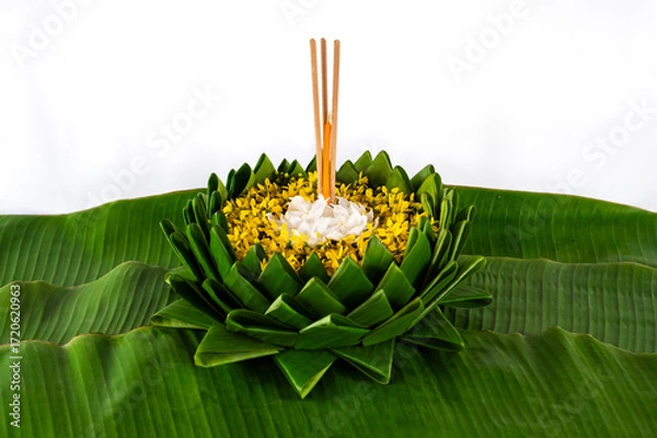 Fototapeta Krathong that have 3 incense sticks and candle decorates with white and yellow flowers puts on banana leaf for Loy Krathong festival on white background.