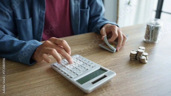 Fototapeta Man calculates finances by calculator Count banknotes and coinsใ