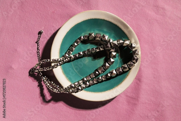 Fototapeta Silver studded chain in ceramic bowl on pink fabric background, modern minimal still life with vintage style touch.