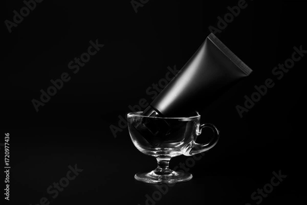 Fototapeta Black plastic cream tube in glass for mockup on black background. Selective Focus.
