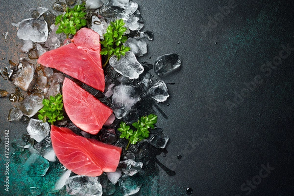 Fototapeta Fresh raw tuna fillet on ice cut into steak on a stone background with seasonings and herbs
