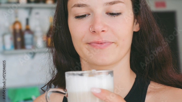 Fototapeta A Young Woman Enjoys a Refreshing Latte Macchiato at a Sunny Bar During a Warm Summer Morning