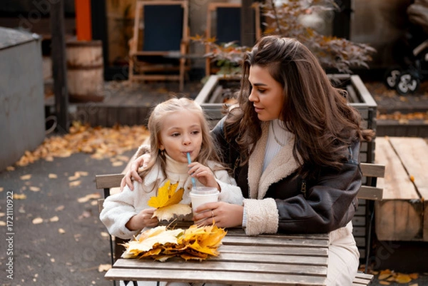 Obraz mom and daughter hug, chat and drink coffee in the cafe in autumn, autumn walk, happy family, maternal love