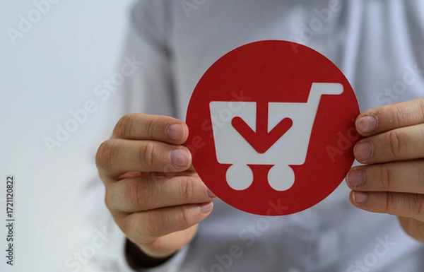 Fototapeta Person holding a red circle with a shopping cart and download arrow. E-commerce, online shopping, purchase concept.