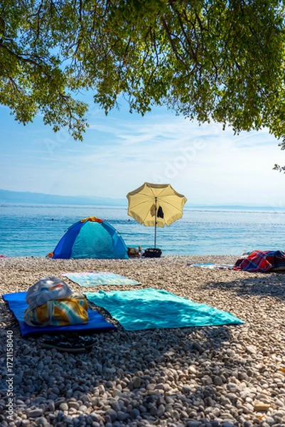 Fototapeta Pebble beach with umbrellas, towels and tent by the calm Adriatic Sea in Croatia